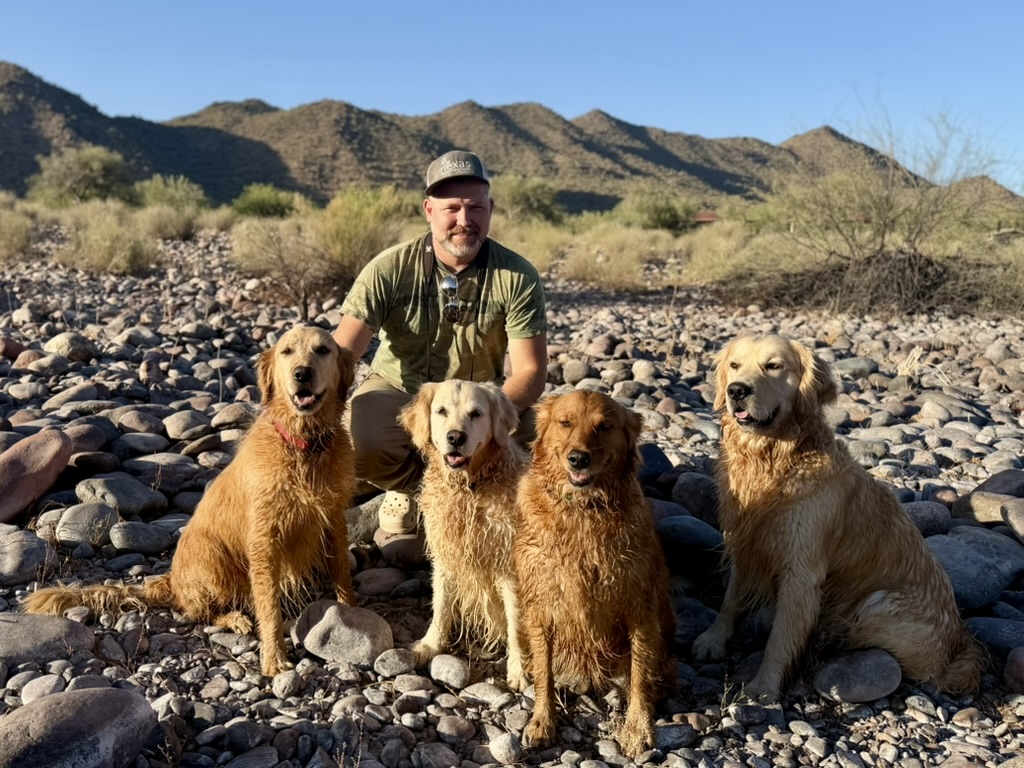 Justin Halls outdoors in the desert with his four golden retrievers